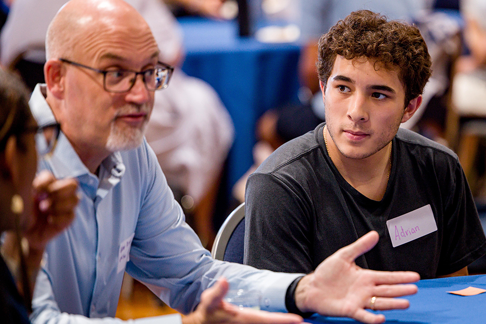 A student and an older male sit at a table during a welcome event.