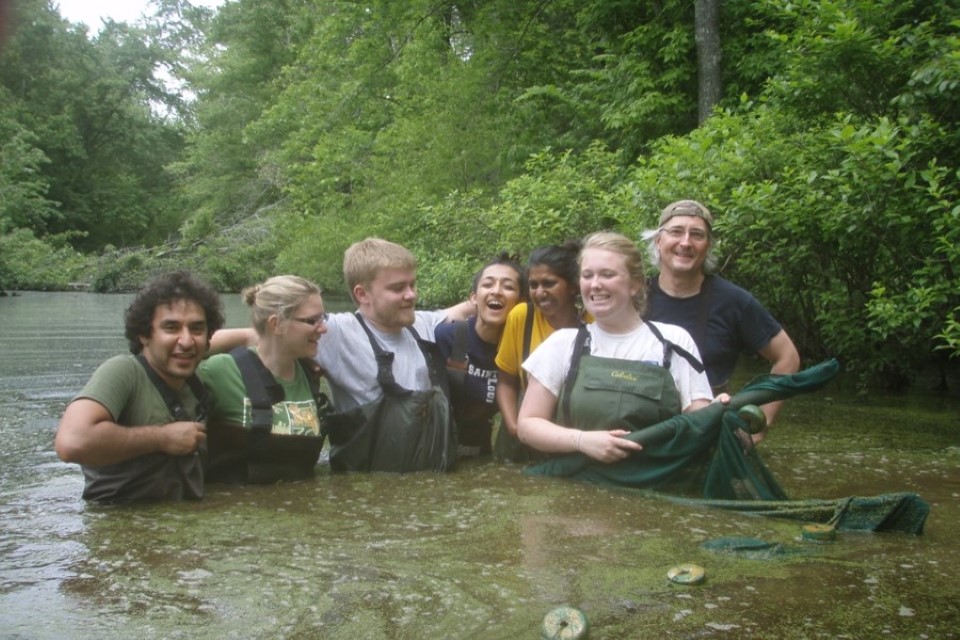 Seven students stand in water, wearing hip waders