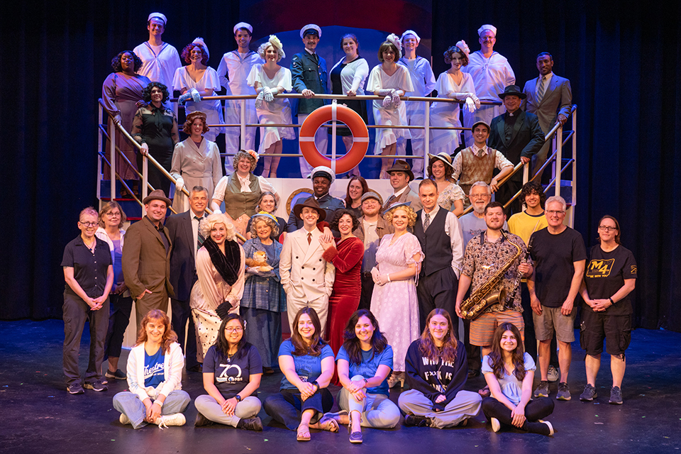 A group of people stand on a theatrical set of a ship