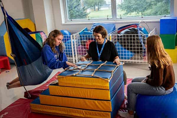 A professor demonstrates how to play a game with two students in an occupational therapy lab.