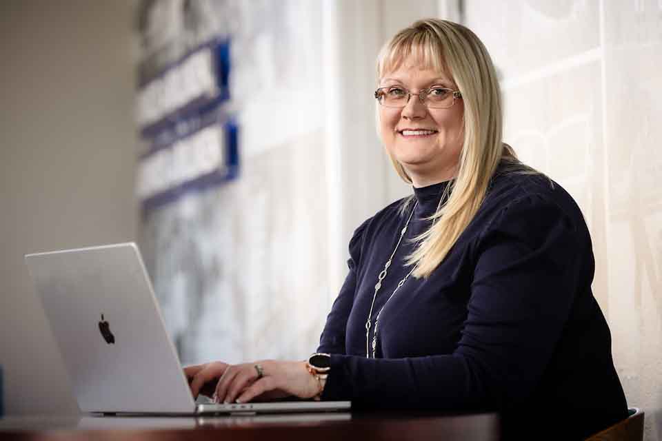 Ann Kelly poses for a photo at a laptop.