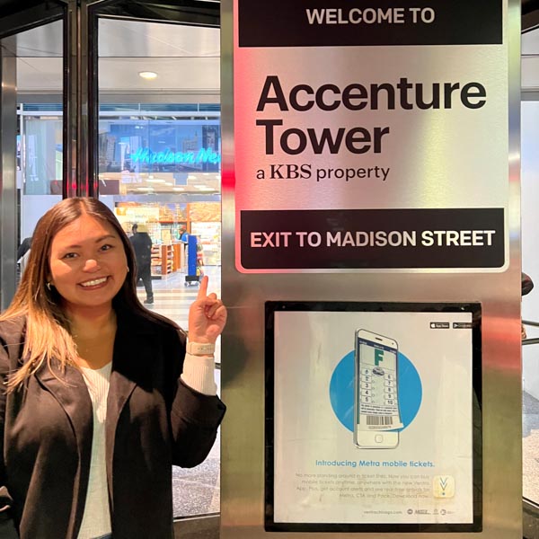 Daniella Soriano pointing to an Accenture Tower sign