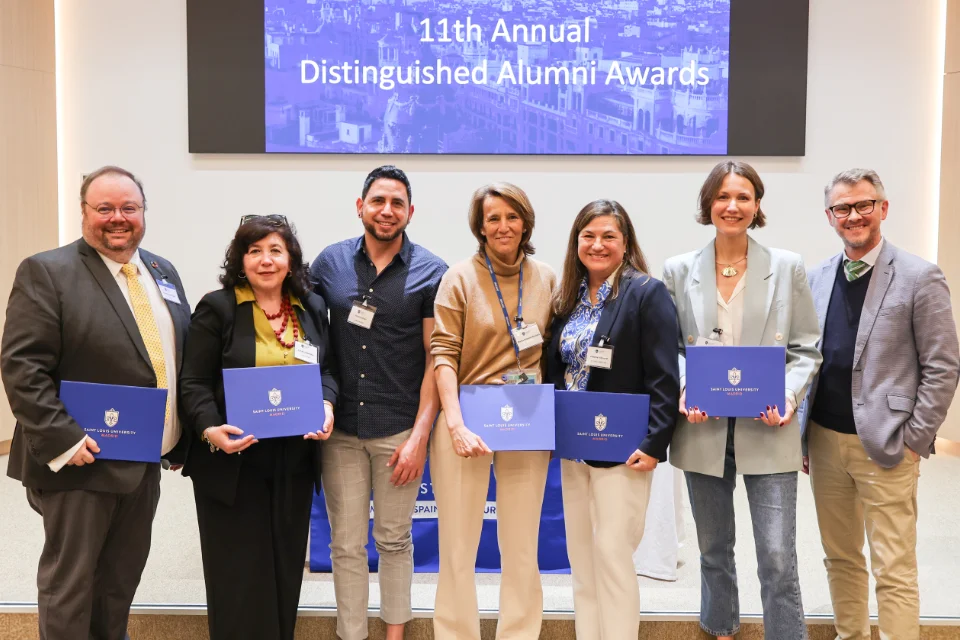 Seven individuals pose for a photo with a screen behind them that reads "11th Annual Distinguished Alumni Awards".