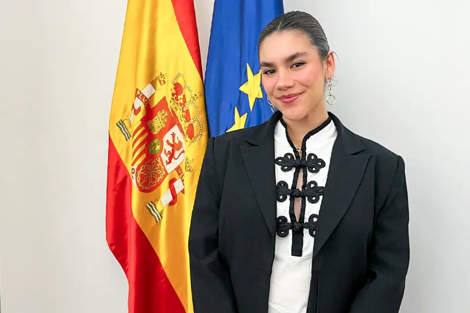 student posing next to the flags of the European Union and Spain.