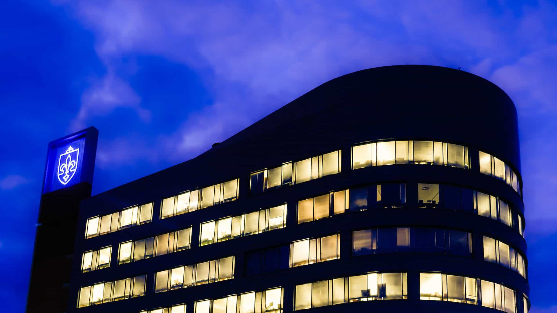 An exterior view of the Doisy Research Center at night. The interior lights illuminate the building’s windows.