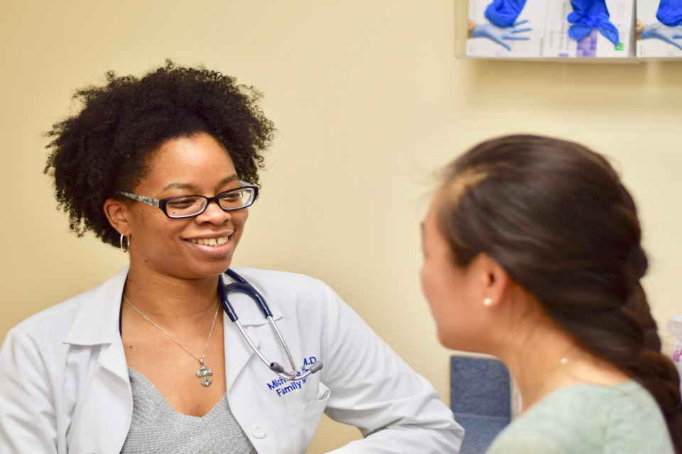 A medical student or resident in a doctor's coat talks to a patient.