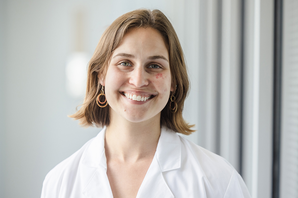 Stella Hoft is shown wearing a white lab coat. She smiles at the camera.