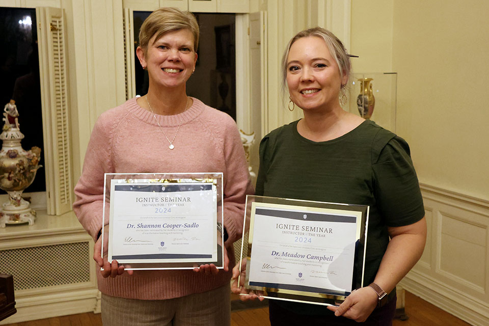 Two female faculty members pose for a photo with their awards.