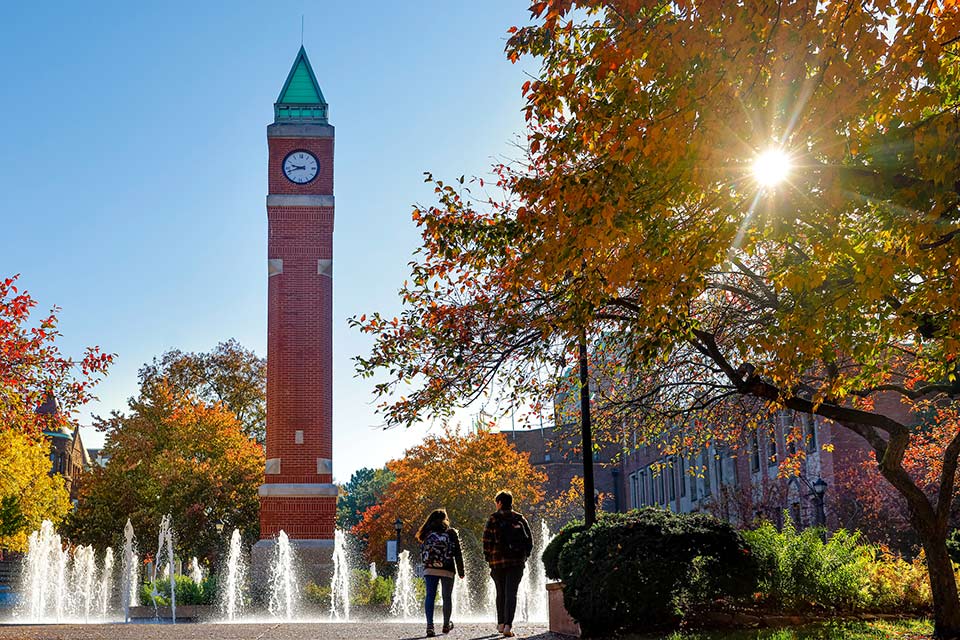 Two students walk by SLU's clock tower on a fall day.