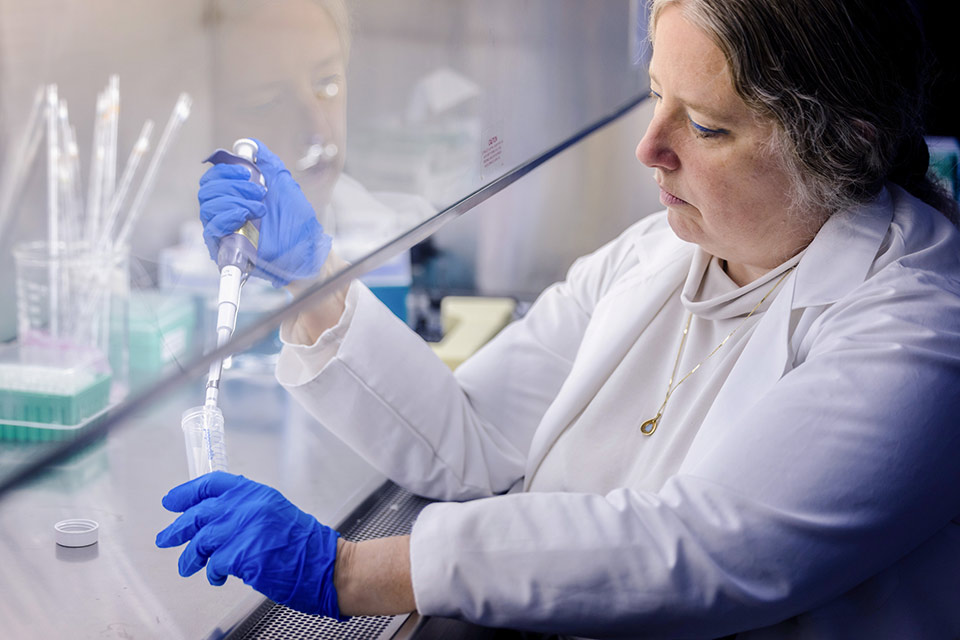 A woman in a lab coat holds a test tube in a laboratory setting.