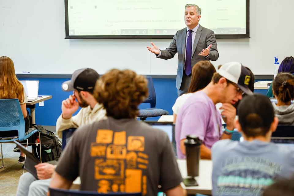 A male professor lectures in front of a full classroom