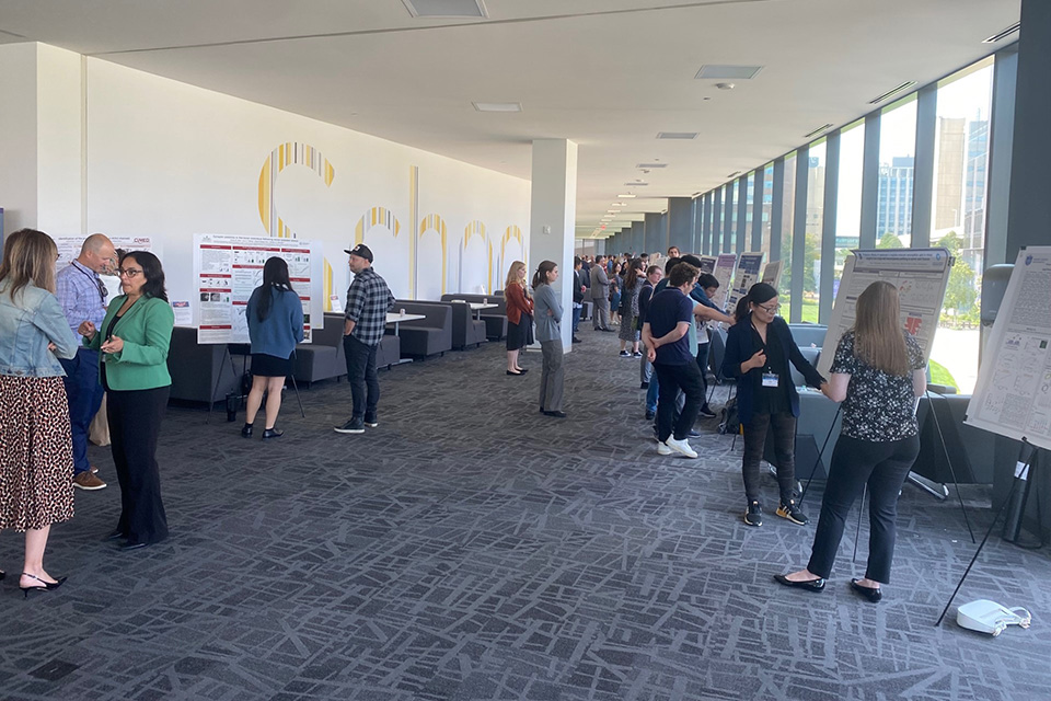 A corridor is lined with easels containing posters, while forum attendees look at the posters and have discussions.