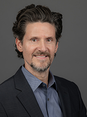 Smiling man in a collared shirt and jacket in front of a blue background